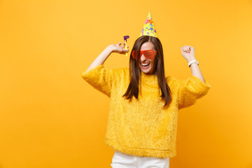 Joyful woman in orange funny glasses birthday party hat with playing pipe rising hands celebrating...