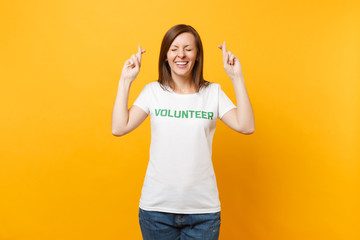 Portrait of happy smiling satisfied woman in white t-shirt with written inscription green title volunteer isolated on yellow background. Voluntary free assistance help, charity grace work concept.