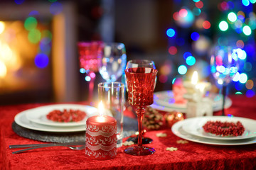 Beautiful table setting for Christmas party or New Year celebration at home. Cozy room with a fireplace and Christmas tree in a background.