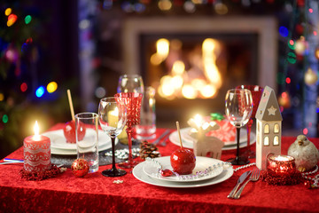 Beautiful table setting for Christmas party or New Year celebration at home. Cozy room with a fireplace and Christmas tree in a background.