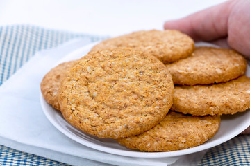 Woman hands holding homemade shortbread cookies made of oatmeal stacked in plate on blue cloth background. Concept food healthy snack for enjoy in holiday. with copy space for text.