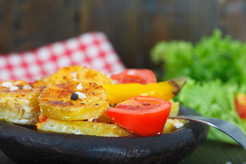 Roasted potato with spices on wooden plate with fork, homemade food. Fresh salad and tomato aside.