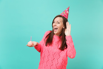 Cheerful young woman in knitted pink sweater, birthday hat eavesdrop, hearing gesture holding in...