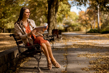 Young woman drinks coffee and using digital tablet in the park