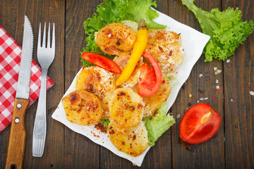 Homemade, roasted potato on white plate. Fresh salad and tomato aside. Top view.