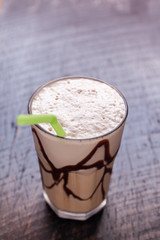 White Frappe Coffee Glass with iced drink with chocolate syrup on a dark wooden table in a cafe.