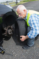 aged man changing leaking tire on the verge