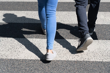 View of pedestrians legs crossing the white zebra crossing line