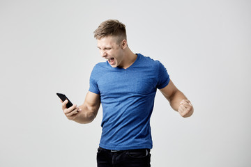 Ecstatic guy dressed in blue t-shirt looks at his mobile phone