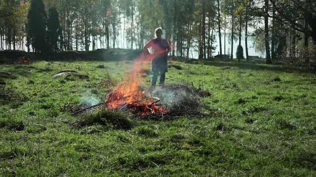 Bonfire in autumn. Bonfire on a meadow to get rid of old bushwood. Woman throwing old branches and leaves on fire. Rural settings in the south of Sweden.