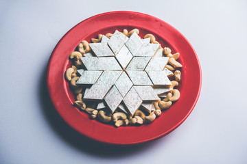 Kaju Katli is a Diamond shape Indian sweet made using cashew sugar and mava, served in a plate or bowl over moody background. selective focus