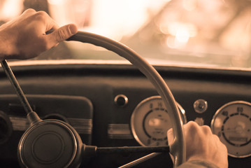 driving a vintage car; only the driver’s hand on the steering wheel are visible, the dashboard is blurred; stylized as an old sepia photo with dust and noise - Powered by Adobe