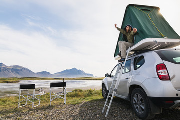 Young bearded man sitting and stretching in a roof top tent mounted on offroad car in Hofn camping site, Iceland © oleksii.leonov