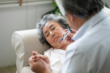 Obraz premium Sick Asian Senior Woman laying on couch while her husband holding and looking to temperature.