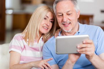 Portrait of a smiling mature couple using digital tablet on sofa at home