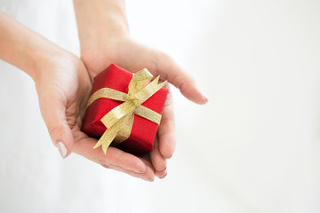 Close up of a hand holding a red gift box tied with a gold ribbon. It is a joy to celebrate the holidays, such as Valentine's Day, Christmas and Happy New Year. The reward for special customers.