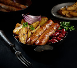 grilled juicy sausages in a pan on a black background
