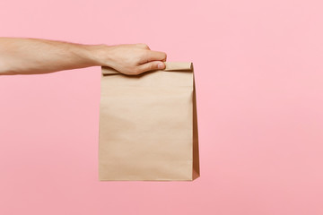 Close up male holding in hand brown clear empty blank craft paper bag for takeaway isolated on pastel pink background. Packaging template mock up. Delivery service concept. Copy space advertising area