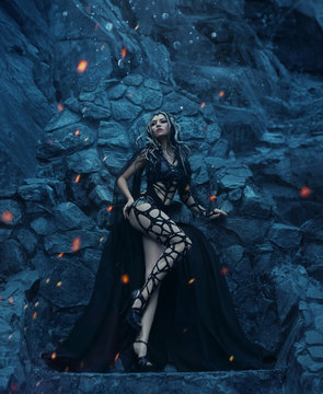 Medusa Gorgona Goddess turning a gaze into a stone. It stands against the background of rocks in cold, blue hues. A girl in a designer costume in the Gothic style, hairpins are golden snakes.