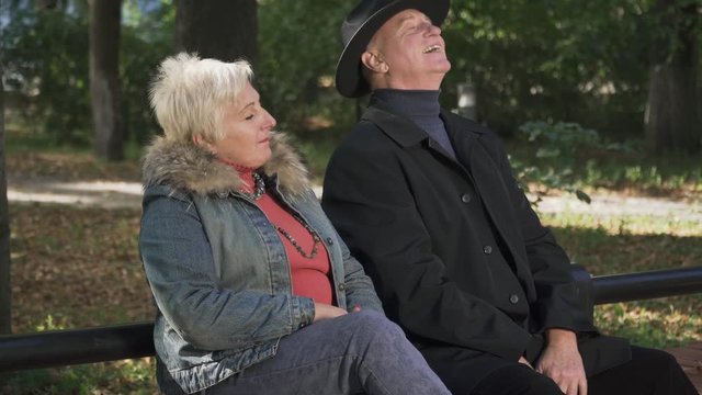 Adult man sits next to an adult woman on a park bench.
