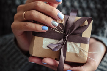 Gorgeous manicure, pastel tender color nail polish, closeup photo. Female hands hold a simple gifts over knit grey background