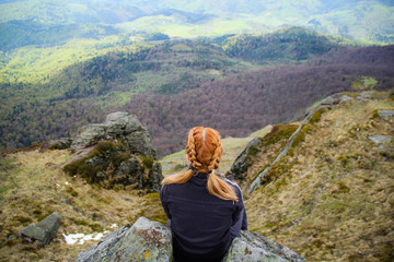 Naklejka na ściany i meble The girl sits on the edge of a cliff with a view of the mountains. Ukrainian Carpathian Mountains. Traveling