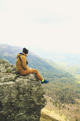 Fototapeta premium The girl sits on the edge of a cliff with a view of the mountains. Ukrainian Carpathian Mountains. Traveling