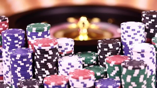 Poker Chips on gaming table, roulette wheel in motion