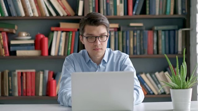 Charming male student making research for startup project using internet information from laptop device in university library, hipster man typing email for asking job vacancy via app on netbook