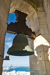 Fototapeta premium A church bell from the cathedral of Cadiz in the center of the frame suspended in its arched opening.