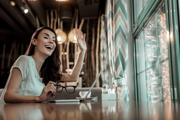 Here I am. Joyful young woman waving hand while having meeting with her friend