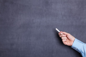 A man's hand holding a piece of white chalk next to a blackboard