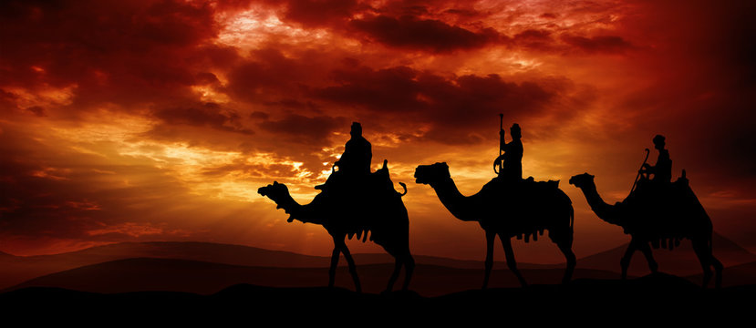 Three kings - traveling in the desert against the background of red clouds rising from the sun
