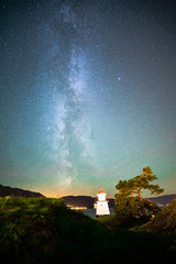 Naklejka na ściany i meble Beautiful Night Sky Milky Way Stars Galaxy with Lighthouse on Ocean Water Coast in Norway Scandinavia