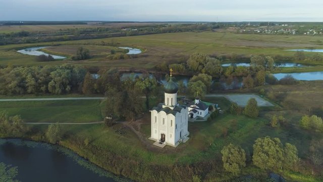 White Church of the Intercession on the Nerl River at Sunny Evening. Vladimir Region, Russia. Aerial View. Drone is Orbiting Around, Camera is Tilting Down