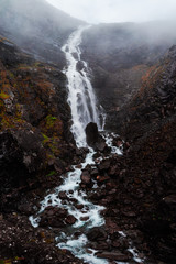 Huge Rushing Waterfall with Foggy Mountain View in Norway with Clouds and Hazy Atmosphere