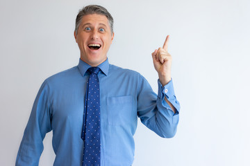 Excited businessman overjoyed with brilliant idea. Middle aged Caucasian man with open mouth raising finger up and pointing at copy space. Eureka concept