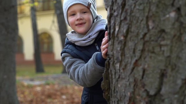 Childhood, season and people concept - beautiful little girl hiding behind tree in autumn