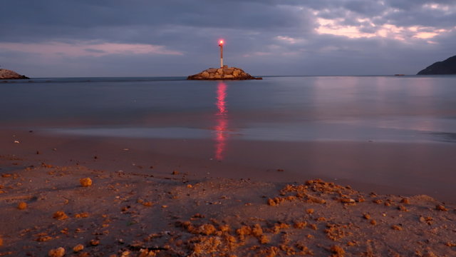 Lighthouse shining on an island on the shore of the beach with the reflection of light in the water at sunset on a cloudy day in Benidorm, Spain