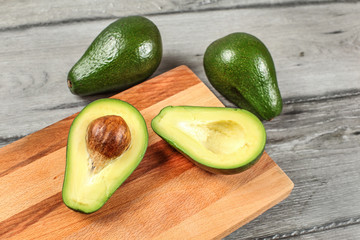 Avocado on wooden chopping board cut in half, seed visible, whole green avocado pears in background.