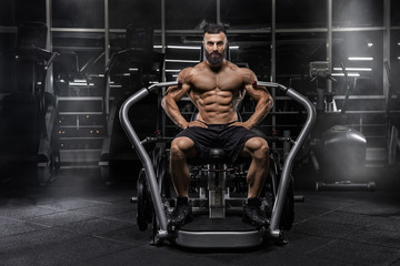 Fototapeta na wymiar Young handsome male athlete bodybuilder weightlifter with idial abdominals, doing exercises in modern gym on a dark background. Exercises for biceps. 