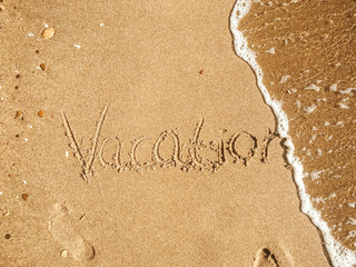 Vacation text written on sandy beach with wave near sea. Summer vacation concept. Hello summer. Travel and wanderlust. Space for text. Happy holidays. Time to relax
