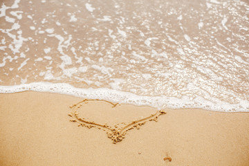 Heart written on sandy beach with wave near sea. Love concept. Happy valentine's day.  Honeymoon for newlyweds. Valentine day. Space for text. Happy holidays. Broken heart