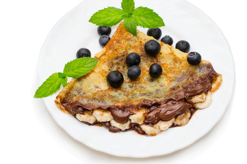 homemade crepes with chocolate cream, banana and blueberries on white background. pancakes