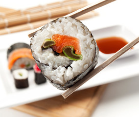 Detalle en primer plano de unas pinzas sujetando un rollo de sushi