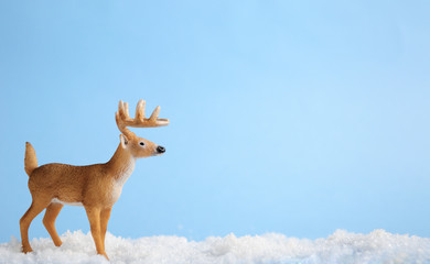 Toy horned deer stands on artificial snow on blue background. Concept animals in the winter, children's toys, winter billboard or advertising.