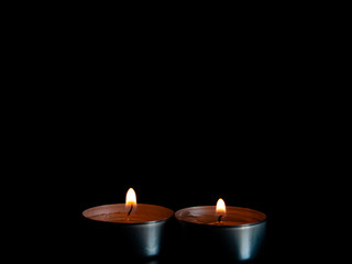 Obraz na płótnie Canvas Two lighted candles with an orange flame and isolated on a black background