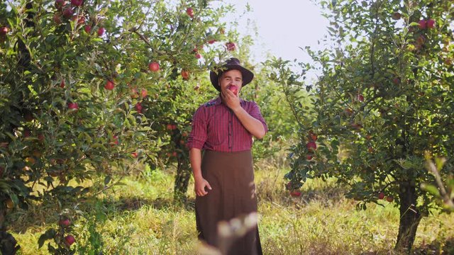 A young farmer eating an apple and showing thumbs to up in the apple garden