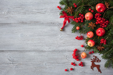 Christmas wooden background with fir branches, red apples, berries and anise