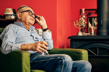 Pensive Jewish senior sitting in the armchair and drinking kosher wine